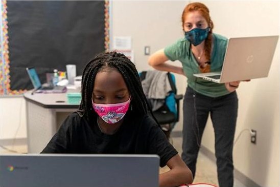 A student works on a laptop while a tutor looks on