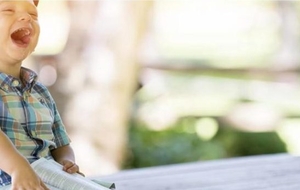 A laughing young boy sitting outdoors with a book