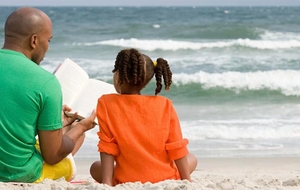 A father and daughter reading at the beach