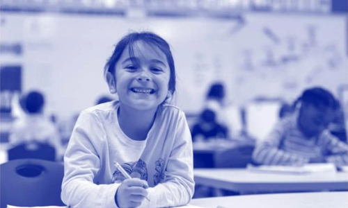 A young girl smiling and writing in a classroom